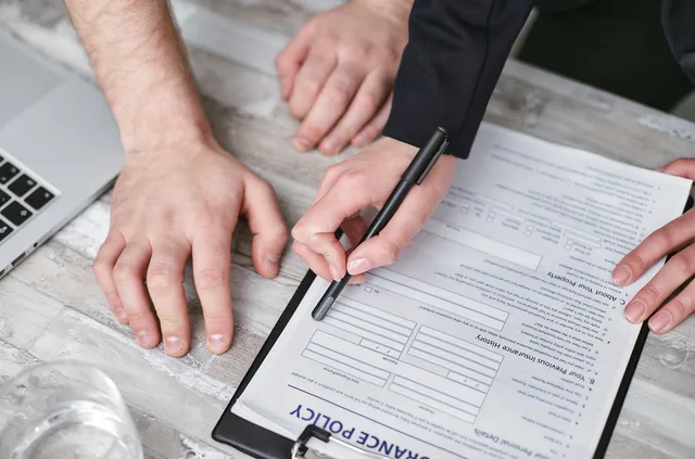 Close-up image of two people signing an insurance policy document on a wooden desk. Business insurance hidden costs beyond the premium: IPT at 12%, fees, finance and excess