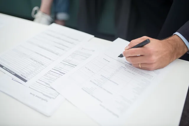 Close-up of a hand signing insurance documents in an office setting. Business insurance operations guide after you buy: certificates, claims, complaints and the FCA register