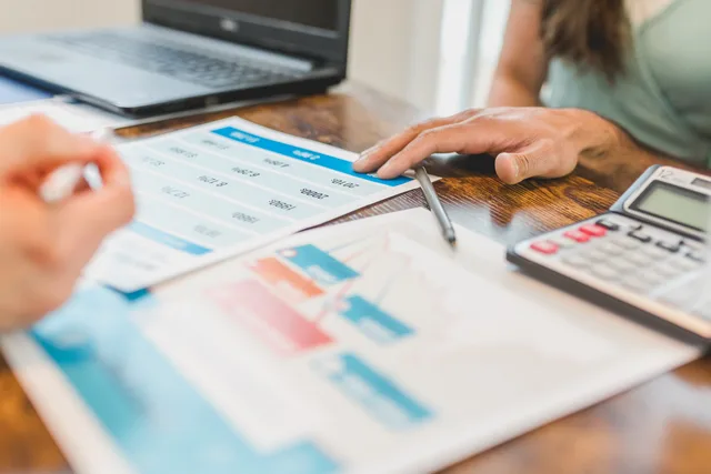 Hands at a desk with financial graphs, calculator, and pen, analyzing business data. Annual, financed, adjustable or packaged? Insurance pricing structures on total cost and timing