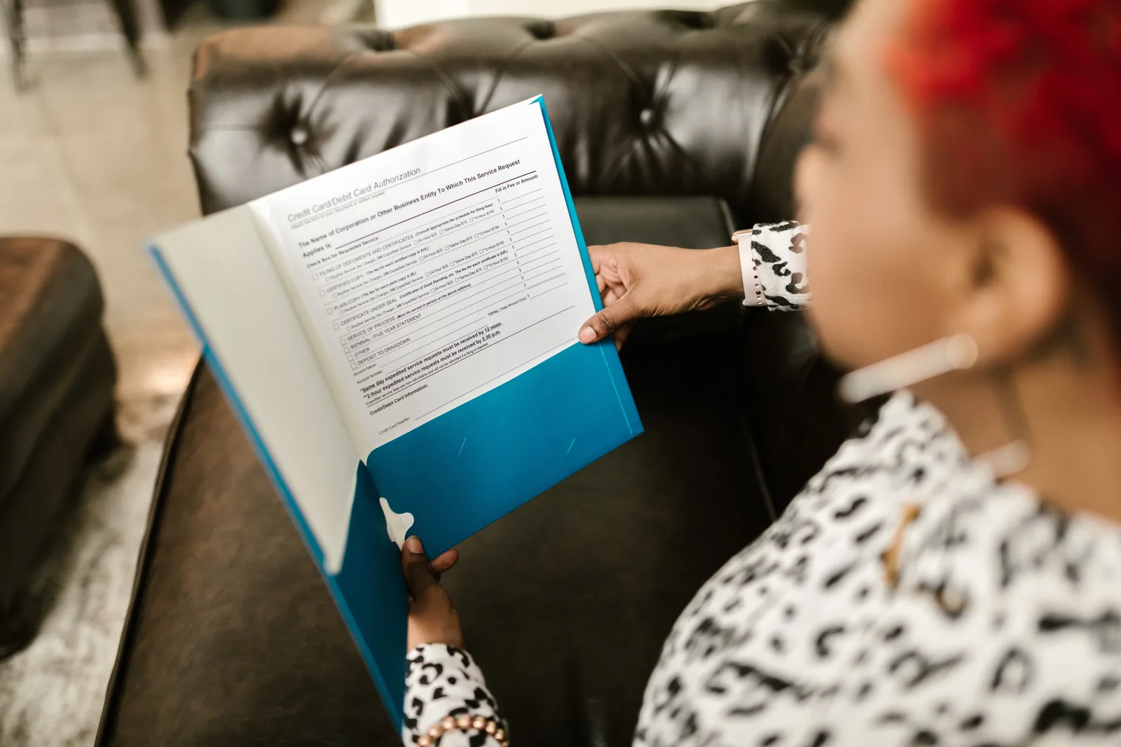 A woman sits on a couch reading a document in a blue folder.