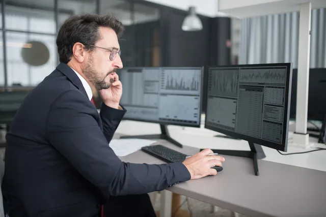 Businessman analyzing stock market data on dual monitors in a modern office setting. Business insurance supplier comparison: software test method